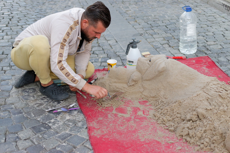 12 - A street artist carving a realistic dog sculpture out of sand on a city pavement